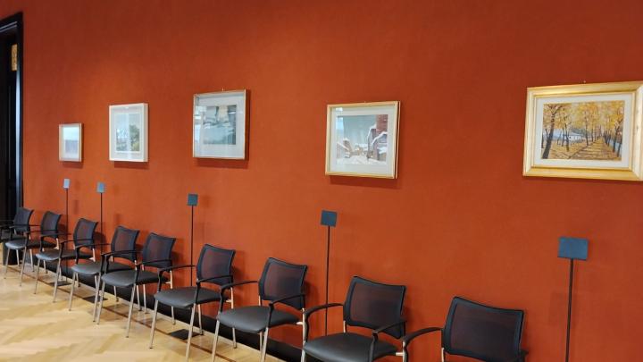 Dipinti di paesaggio esposti su una parete rossa al di sopra di una fila di sedie d'ufficio 