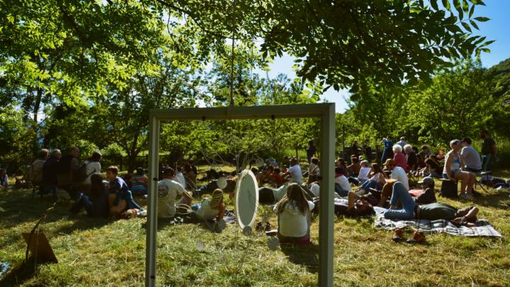 Prato con effetto di sole, persone sedute sull'erba e gong in primo piano