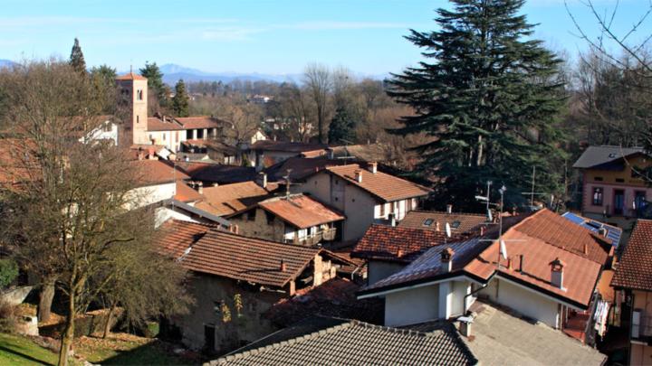 Panorama di Comignago. Foto di Alessandro Vecchi da Wikipedia Case e chiesa con campanile tra alberi