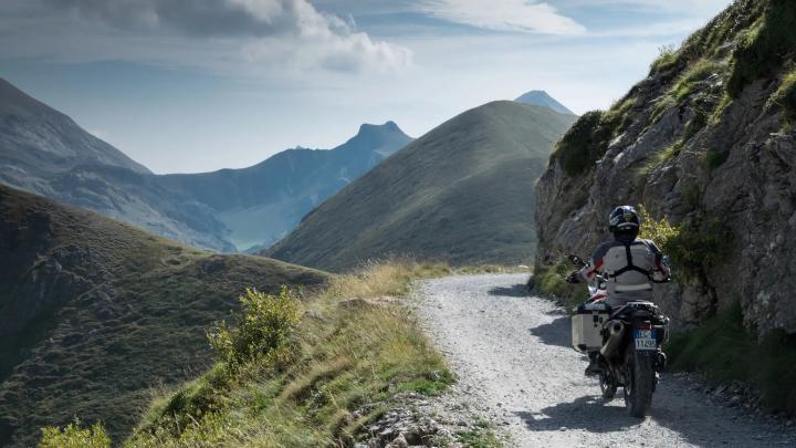 Fotografia dal sito www.visitcuneese,it Motociclista in corsa su strada sterrata in alta quota fra montagne