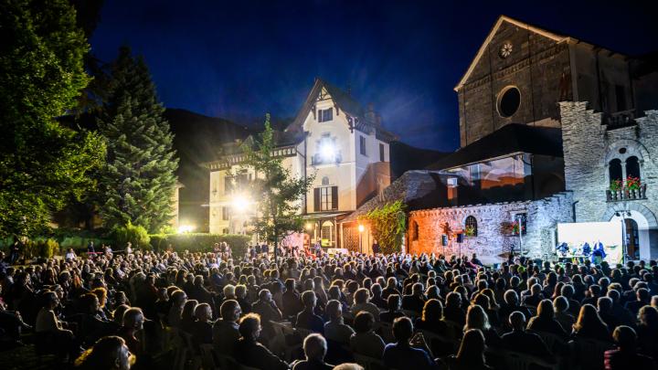 Sentieri e pensieri. Foto di Cristiano Mazzi Incontro pubblico in parco con edifici in pietra, oratori sul palco e spettatori seduti