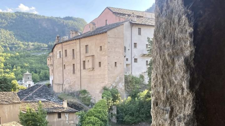 Il complesso del Castello di Adelaide di Susa visto dall'alto attraverso una bifora del campanile di Santa Maria Maggiore, tra i tetti in lose del borgo e la collina.
