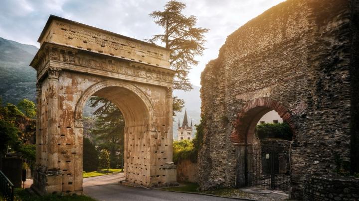 Veduta dell'Arco di Augusto a Susa, monumento romano in pietra, con sullo sfondo la torre del campanile della cattedrale.